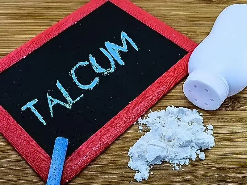 a chalk blackboard with a red frame and the word "Talcum" written on it, next to a pile of baby powder